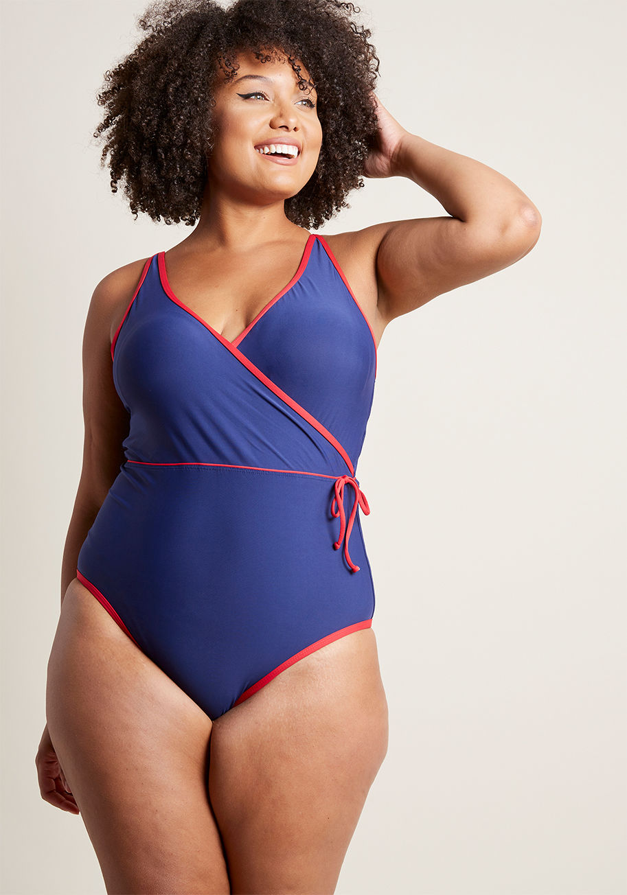 MC0932 - Right up there with the sunscreen and your fave pair of shades, this navy swimsuit is a getaway essential! A High Dive by ModCloth maillot, this classic one piece - with its surplice top, accompanying decorative side tie, scooped back, and bright red trim