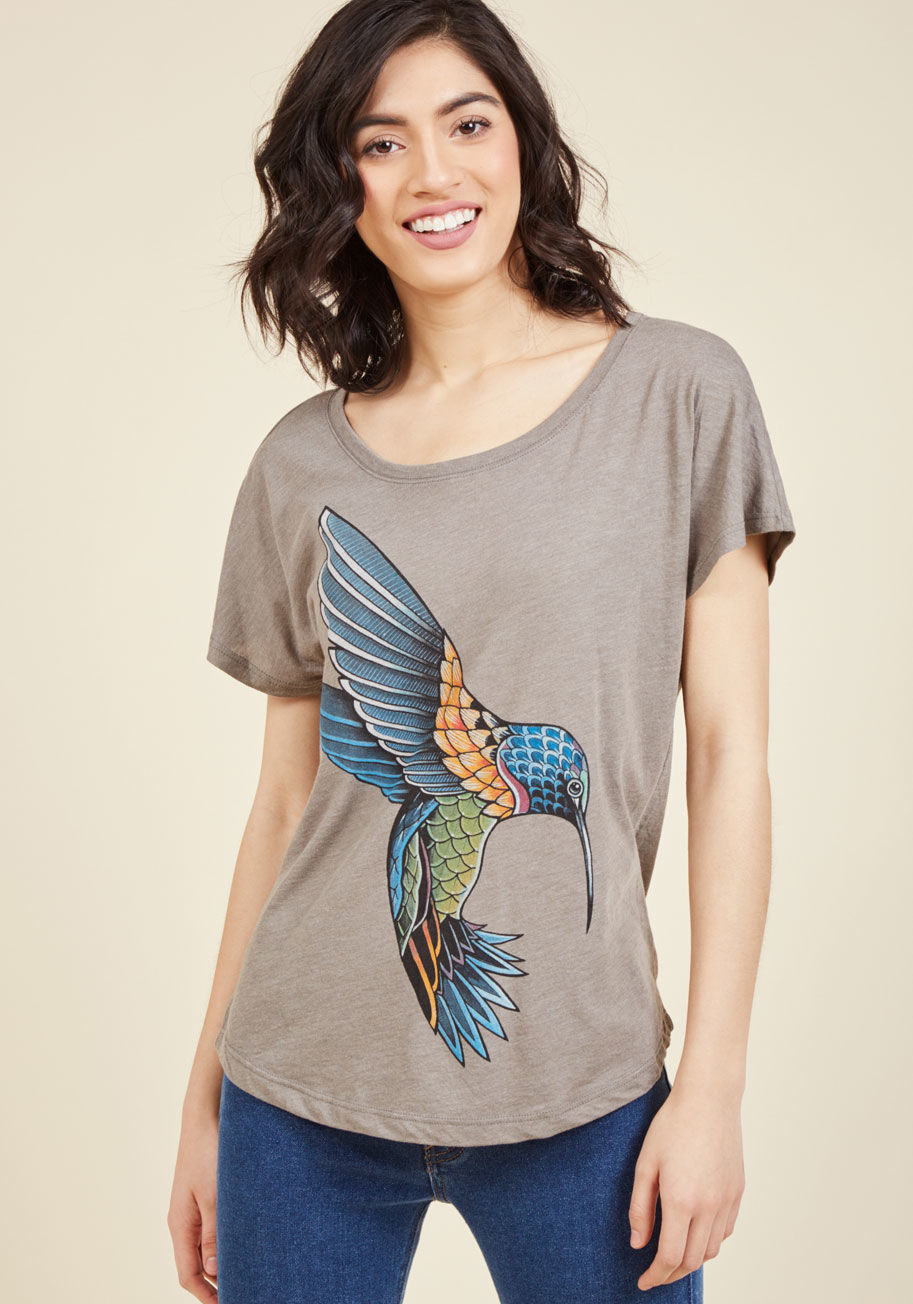  - A comfy grey top characterized by an eye-catching hummingbird graphic? Yeah, this tee's got it, but that's just the beginning! Further equipped with a wide neckline, seamless short sleeves, and a jewel-toned collection of sapphire, red-orange, jade green,