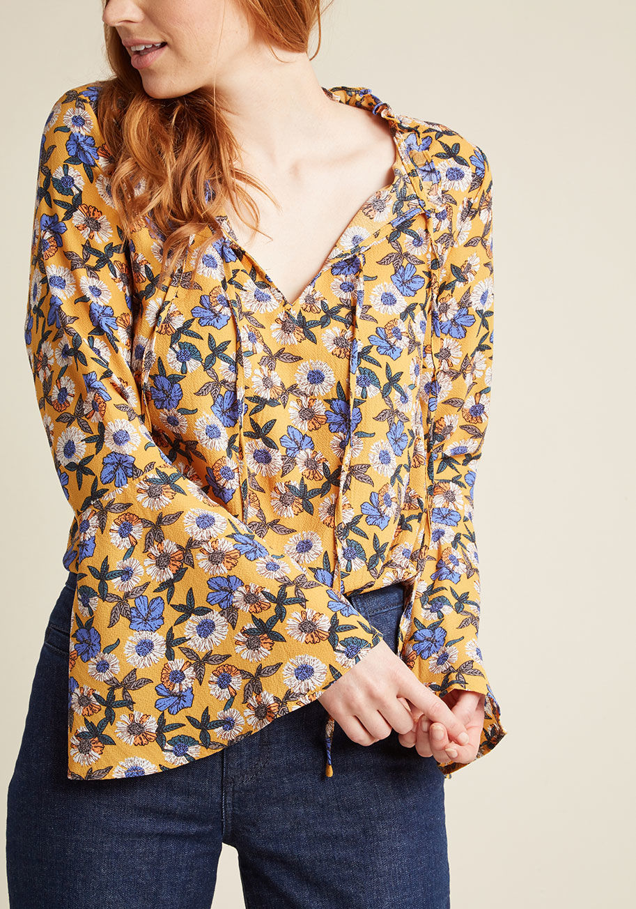  - The throwback bliss you'll experience from flaunting this mustard yellow blouse isn't limited to its debut wear! With its ruffled neckline situated snugly atop a pair of ties, beautiful bell sleeves, and fun floral print