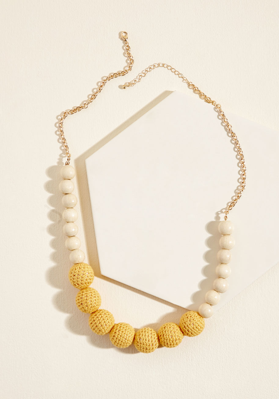 When something tells you it's time to rock this statement necklace, you listen to that notion! Adjusted behind your neck with golden cable chains, this eye-catching piece showcases blond wood beads and mustard crocheting-covered baubles that bring an elem by 456450N-101