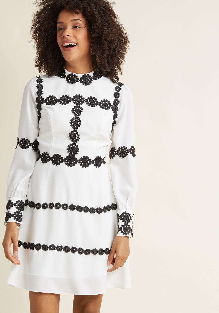 AFA3556 - Contouring your beautiful frame with crocheted black flowers, this long-sleeved white dress introduces loveliness to every aspect of your look. With a haute high neckline, flattering princess seams, and sleeve cuffs fastened with pearl-inspired buttons, t