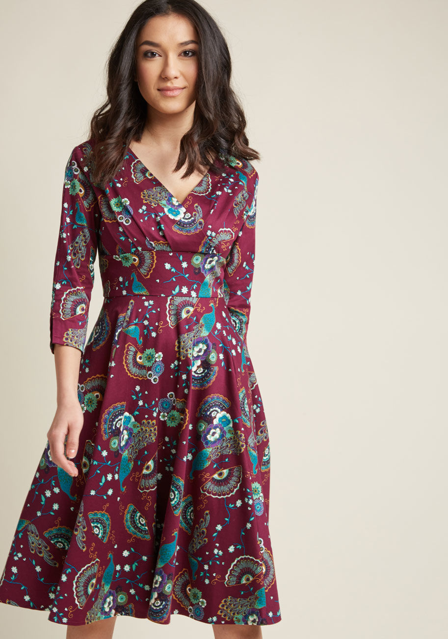 This 3/4 sleeve dress is one sure way to make a statement! Rocking a pleated surplice neckline, a broad waistband, vented sleeves, and an A-line silhouette, this stretch-cotton beauty is radiantly retro. Plus, the teal, purple, and gold fans, florals, and by DR5362